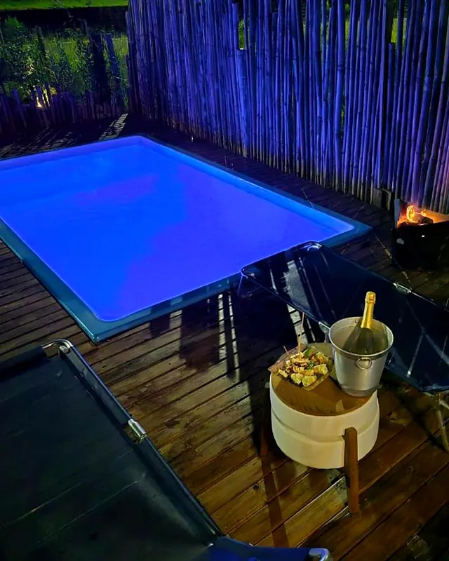 A piscina da Casa Container à noite, iluminada de azul, com o deck de madeira em volta
