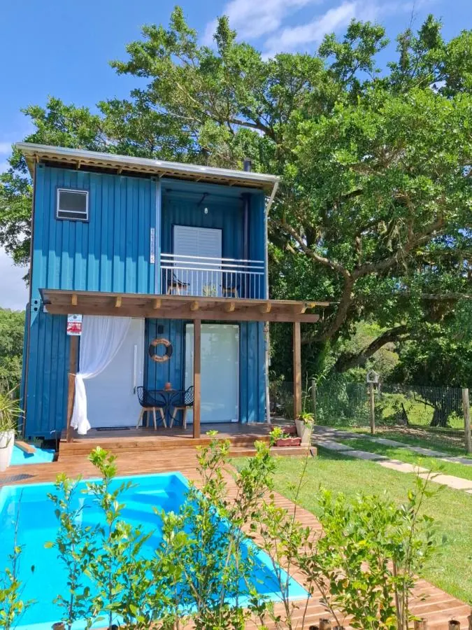A Casa Container: a casa de container azul, de dois andares, com a figueira atrás e a piscina na frente